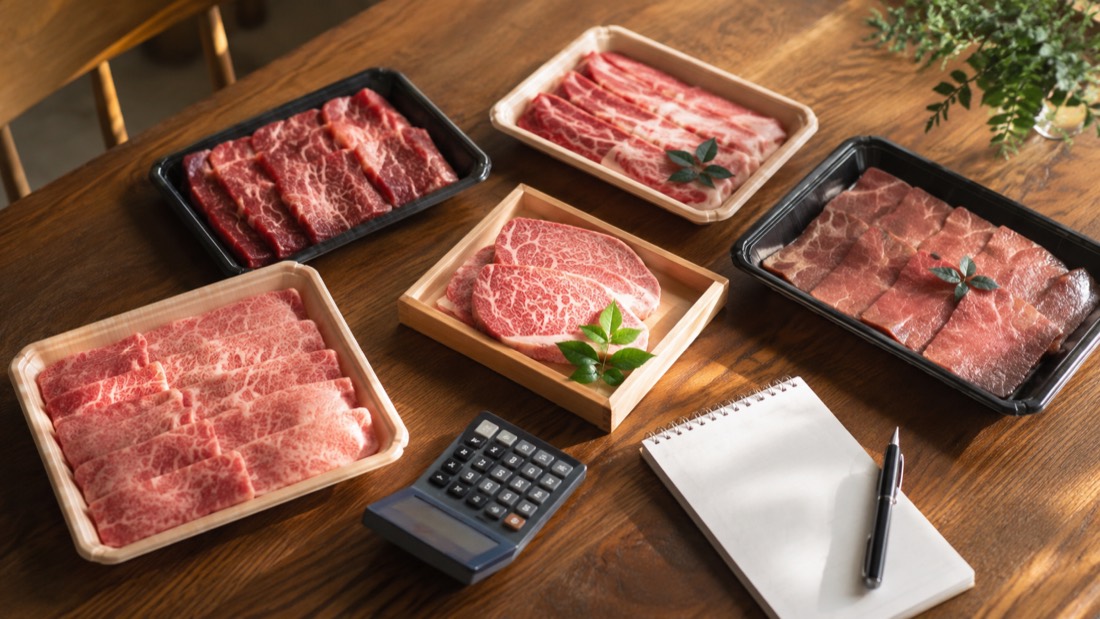 焼肉用の肉のパックと電卓、メモ帳を並べて予算を考えながら返礼品を選ぶイメージ
