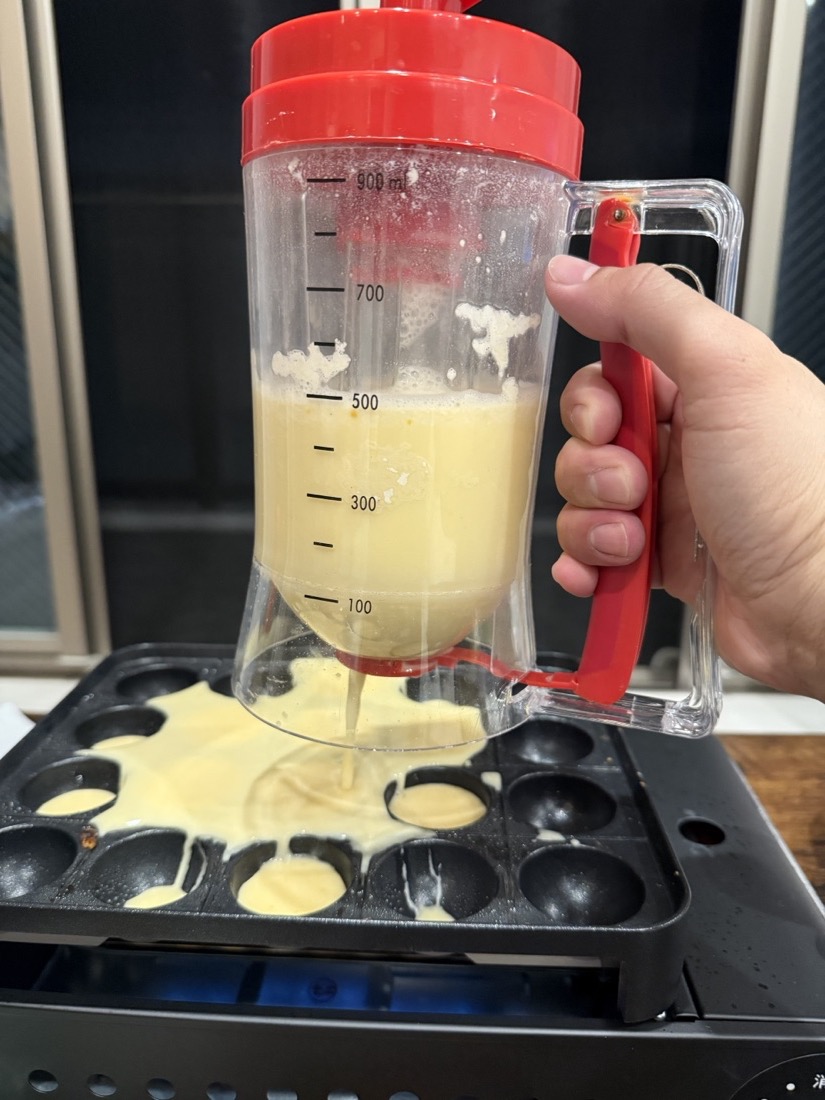 レバー式の粉つぎ器でたこ焼きプレートの穴に生地を注いでいるところ